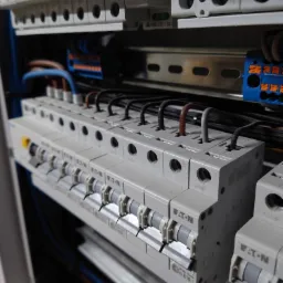 Szczegółowe ujęcie rozdzielnicy elektrycznej z zamontowanymi bezpiecznikami marki Eaton, widoczne przewody w różnych kolorach podłączone do zabezpieczeń, szyna montażowa i oznaczenia na obudowach.