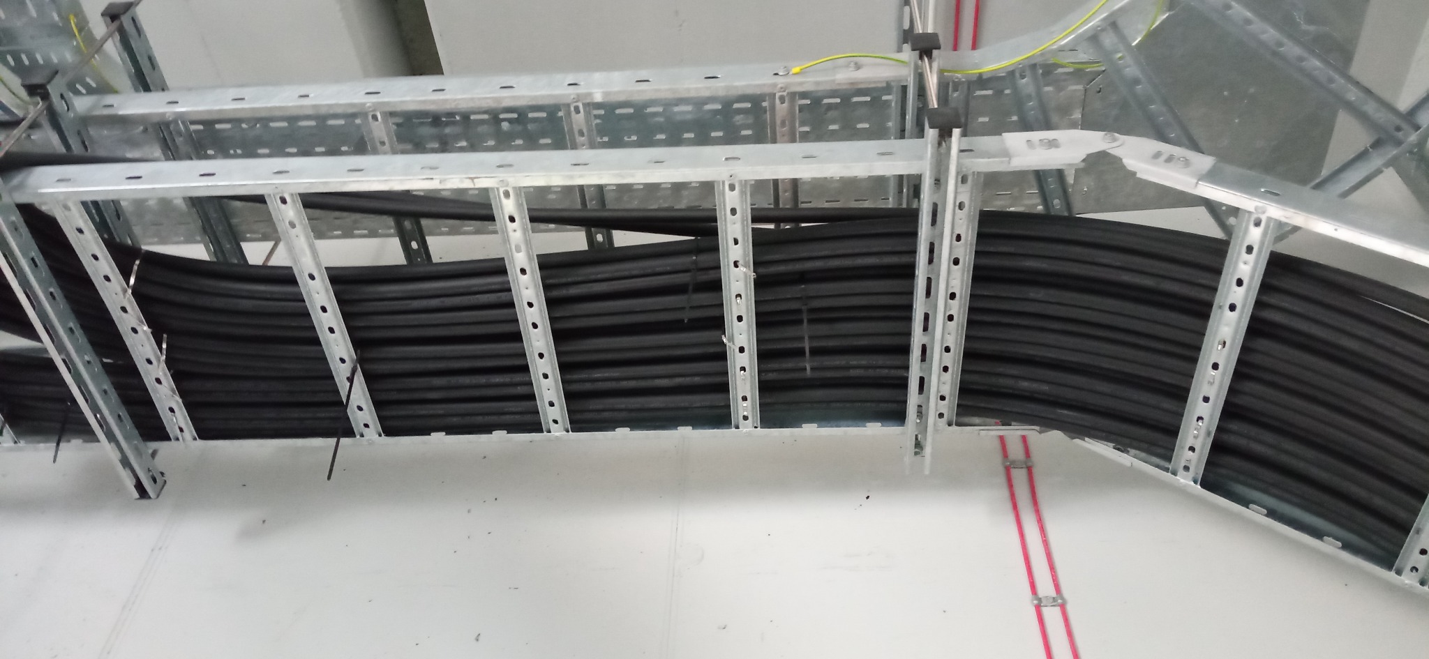 Rząd czarnych kabli ułożonych w metalowej korycie kablowej pod sufitem, zabezpieczone opaskami zaciskowymi.