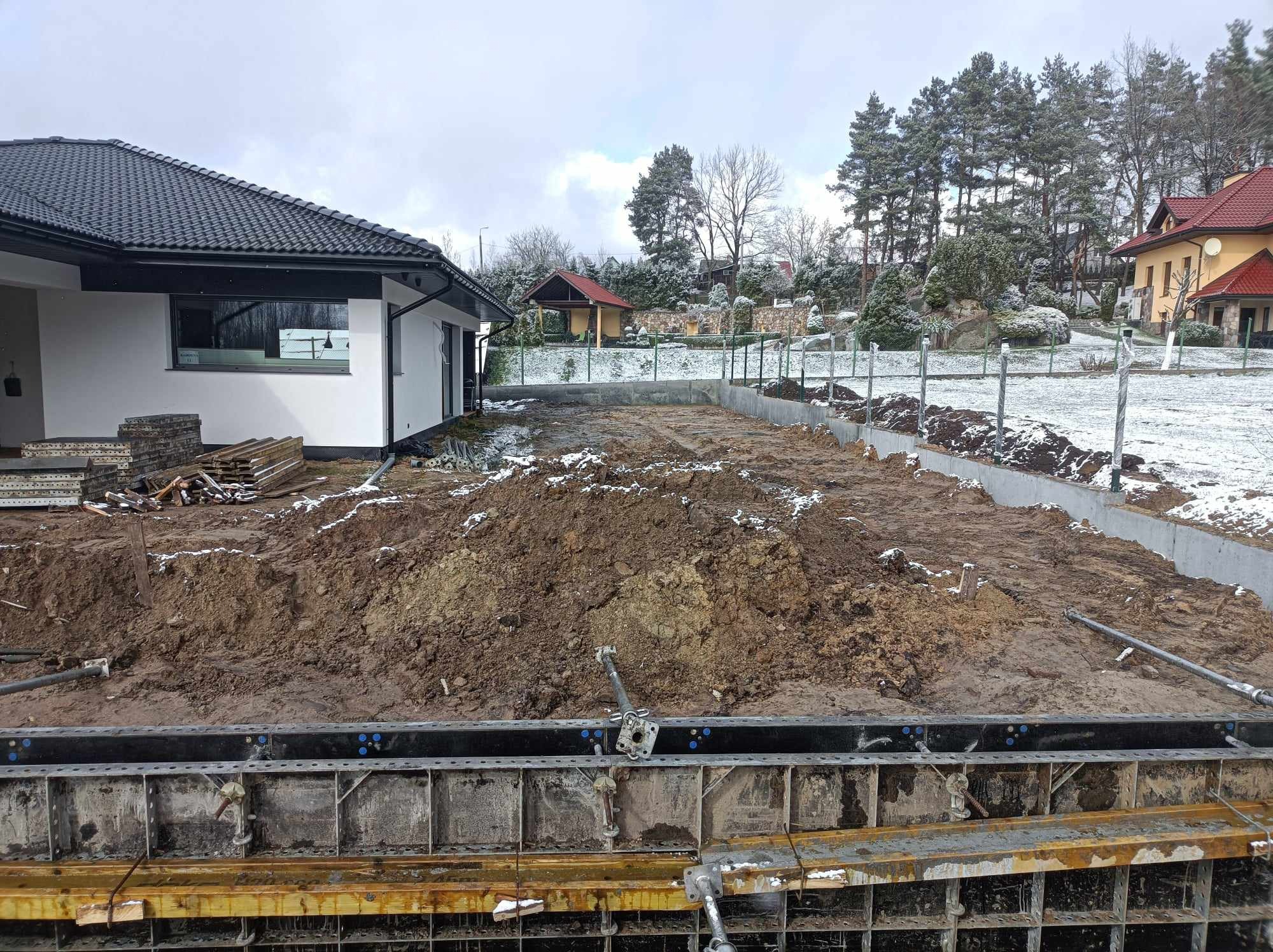 Przygotowanie terenu pod wylewkę fundamentów domu jednorodzinnego, widoczne szalunki i częściowo odśnieżona ziemia.