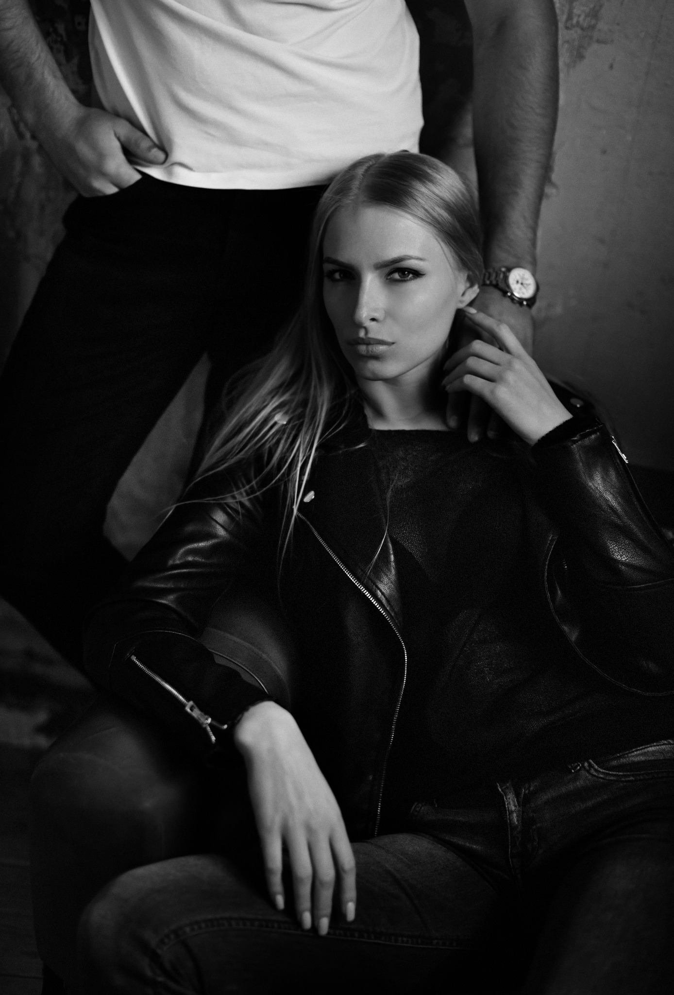 Czarno-białe portretowe ujęcie kobiety w skórzanej kurtce, siedzącej w fotelu, z mężczyzną w tle, zdjęcie wykonane w Lublinie.