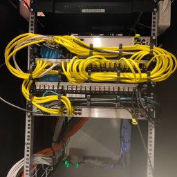 Fest-Instal - Szafa rack z uporządkowanymi kablami sieciowymi, głównie w kolorze żółtym, zabezpieczonymi czarnymi opaskami, widoczne przełączniki sieciowe i patch panele, z etykietami i diodami LED.