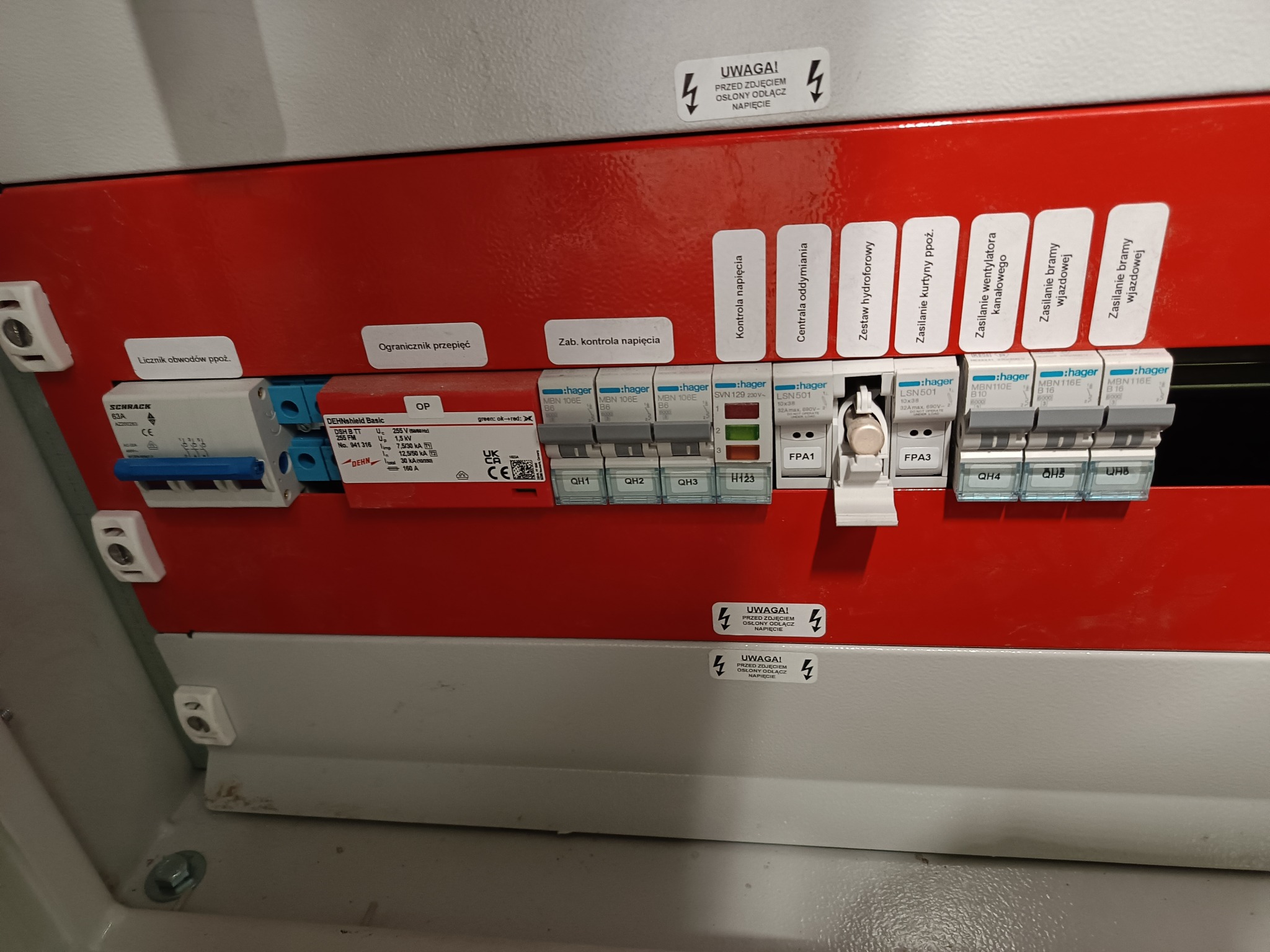 Rozdzielnica elektryczna z bezpiecznikami i zabezpieczeniami, widoczne oznaczenia obwodów, ograniczniki przepięć, kontrola napięcia, zasilanie kurtyny ppoż. i wentylacji kanałowej, naklejki...