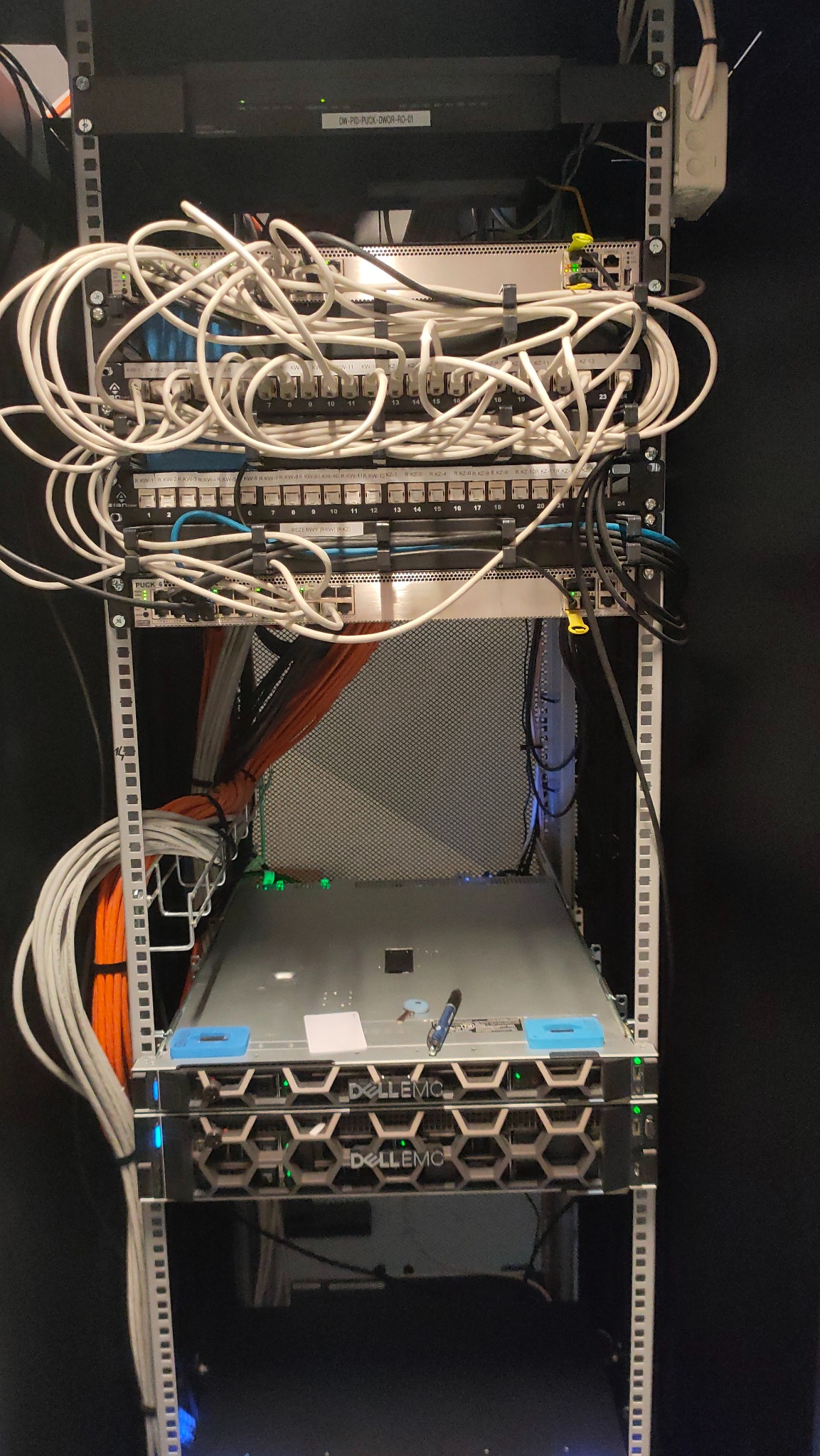 Szafa serwerowa z widocznymi serwerami Dell EMC, panelami krosowniczymi i plątaniną kabli sieciowych, niektóre uporządkowane w wiązki; widoczne diody LED sygnalizujące pracę urządzeń.