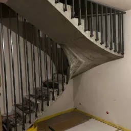 Surowe, betonowe schody z metalową balustradą w trakcie prac wykończeniowych, zabezpieczone kartonem i folią malarską.