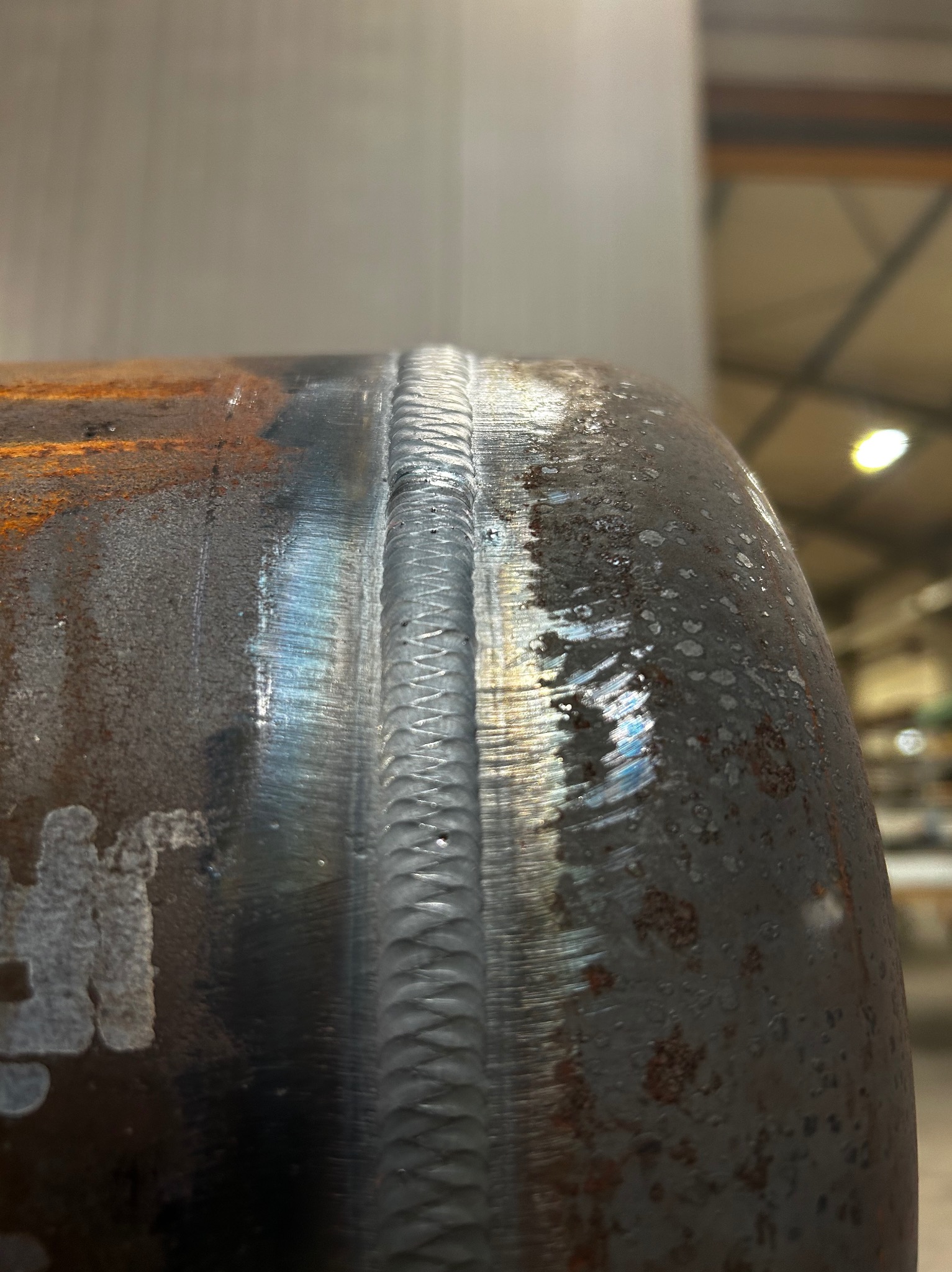 Szczegółowe zbliżenie na spaw na zardzewiałej metalowej rurze, ukazujące precyzję wykonania i strukturę spoiny w warsztacie.