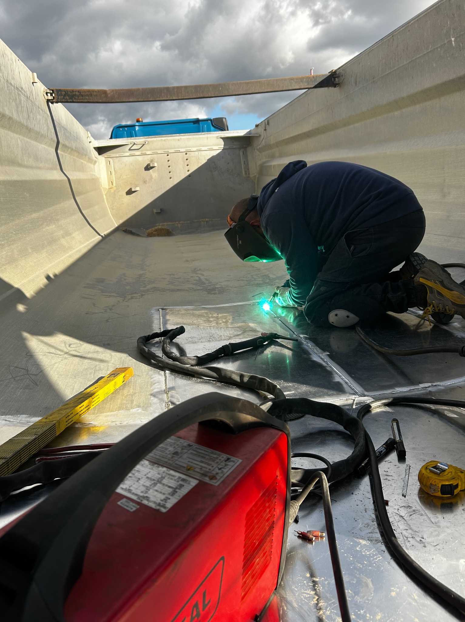 Praca spawacza w Skwierzynie przy naprawie metalowej naczepy ciężarówki, widoczny spawacz w masce, spawarka, przewody i narzędzia.