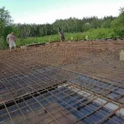 Siatka zbrojeniowa na fundamencie, dwóch pracowników w tle, widok z góry na przygotowanie pod wylewkę.