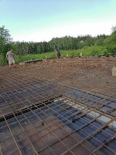 Siatka zbrojeniowa na fundamencie, dwóch pracowników w tle, widok z góry na przygotowanie pod wylewkę.