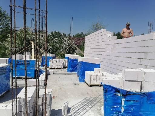 Wznoszenie ściany z bloczków betonu komórkowego Ytong Silka; widoczny zbrojarz bez koszulki na tle muru i palety bloczków w niebieskiej folii.