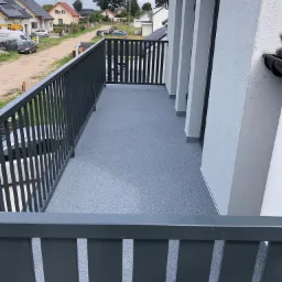 Szary balkon z balustradą, widok na okoliczne domy w słoneczny dzień.