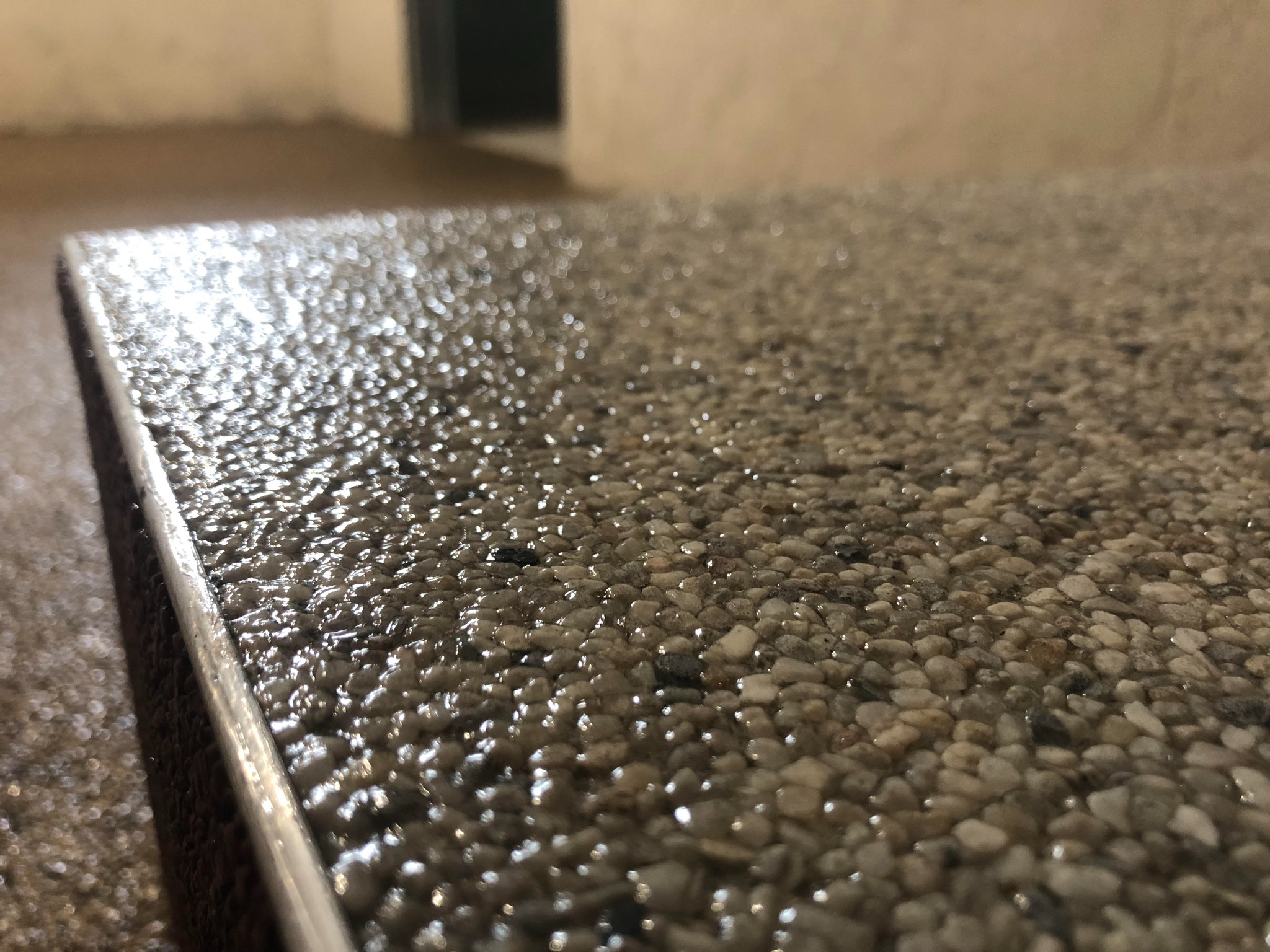 Bliższe ujęcie wykończonej powierzchni podłogi z drobnych kamyczków zatopionych w przezroczystej żywicy, z metalową listwą krawędziową.
