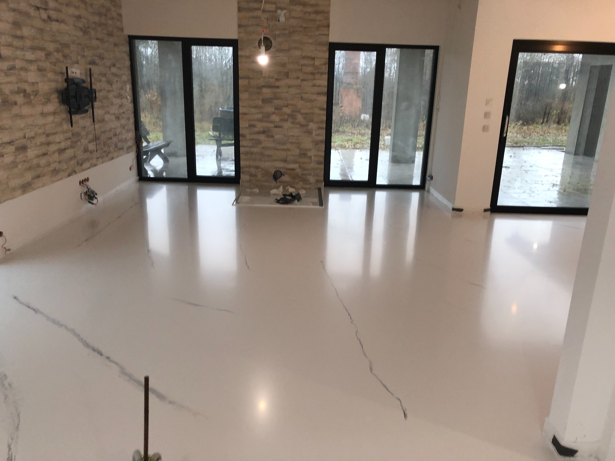 Biała podłoga z żywicy epoksydowej z delikatnymi szarymi żyłkami w przestronnym wnętrzu z dużymi oknami i dekoracyjną ścianą z kamienia.