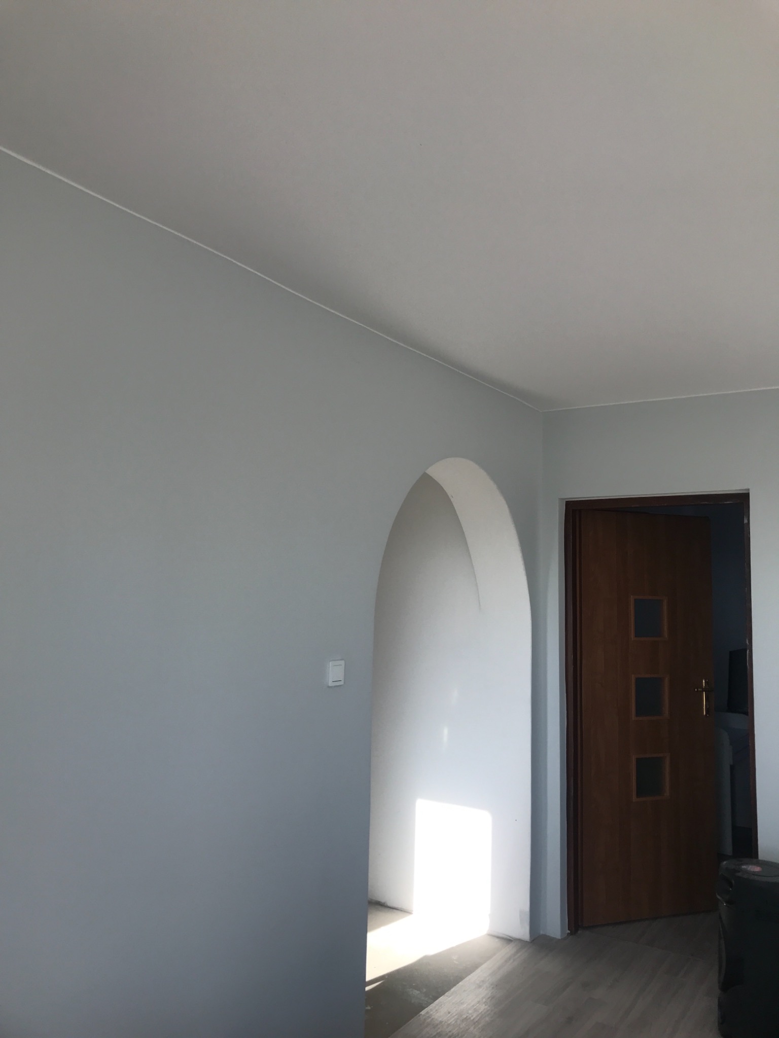 Świeżo pomalowane na szaro wnętrze z drewnianą ościeżnicą i drzwiami z trzema szybkami, widoczny fragment podłogi z paneli.