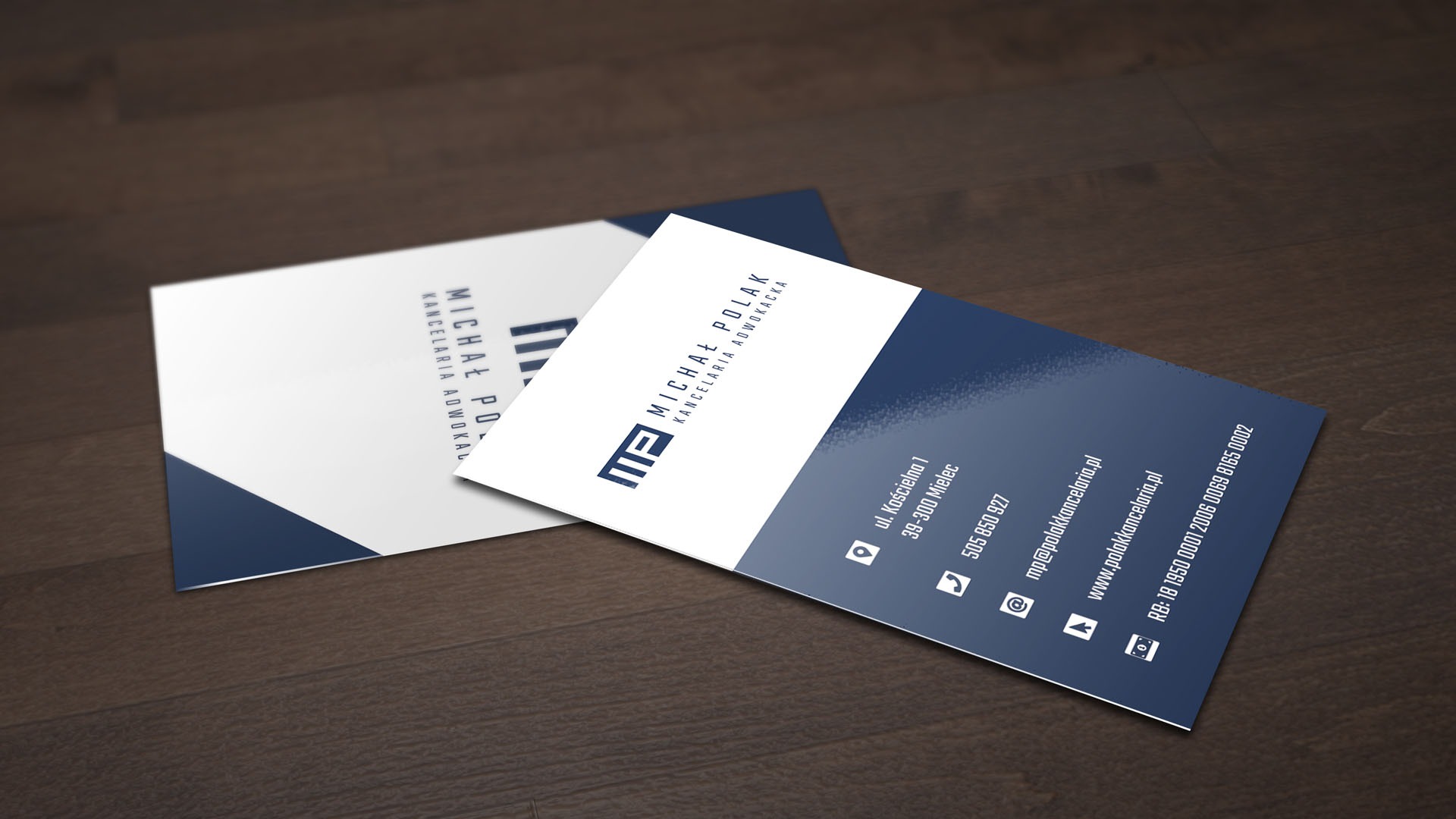 Dwie wizytówki kancelarii adwokackiej Michała Polaka, jedna ustawiona pionowo, druga pod kątem na ciemnym, drewnianym tle. Wizytówki w kolorach bieli i granatu, zawierają logo, dane kontaktowe...