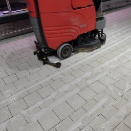 SD-UNION Dariusz Stachowiak - Czerwona maszyna czyszcząca z operatorem w trakcie pracy na jasnej, kafelkowanej podłodze w sklepie, pozostawiająca za sobą mokre ślady.