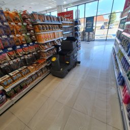 SD-UNION Dariusz Stachowiak - Automat do mycia podłóg w supermarkecie, czyszczący kafelki pomiędzy półkami z towarem, widoczne ślady wilgoci po myciu.