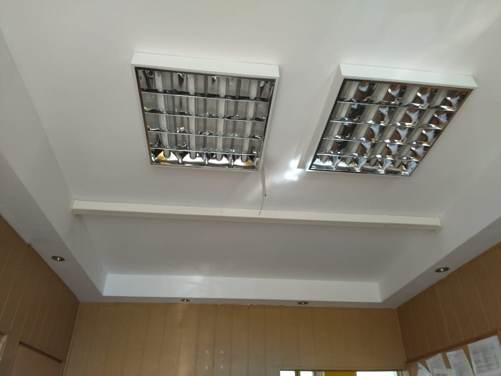 Dwa prostokątne panele oświetleniowe rastrowe zamontowane na białym suficie podwieszanym w biurze, widoczne brązowe panele ścienne.