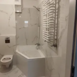 Nowoczesna łazienka z narożną wanną, grzejnikiem drabinkowym i marmurowymi płytkami na ścianach oraz podłodze.