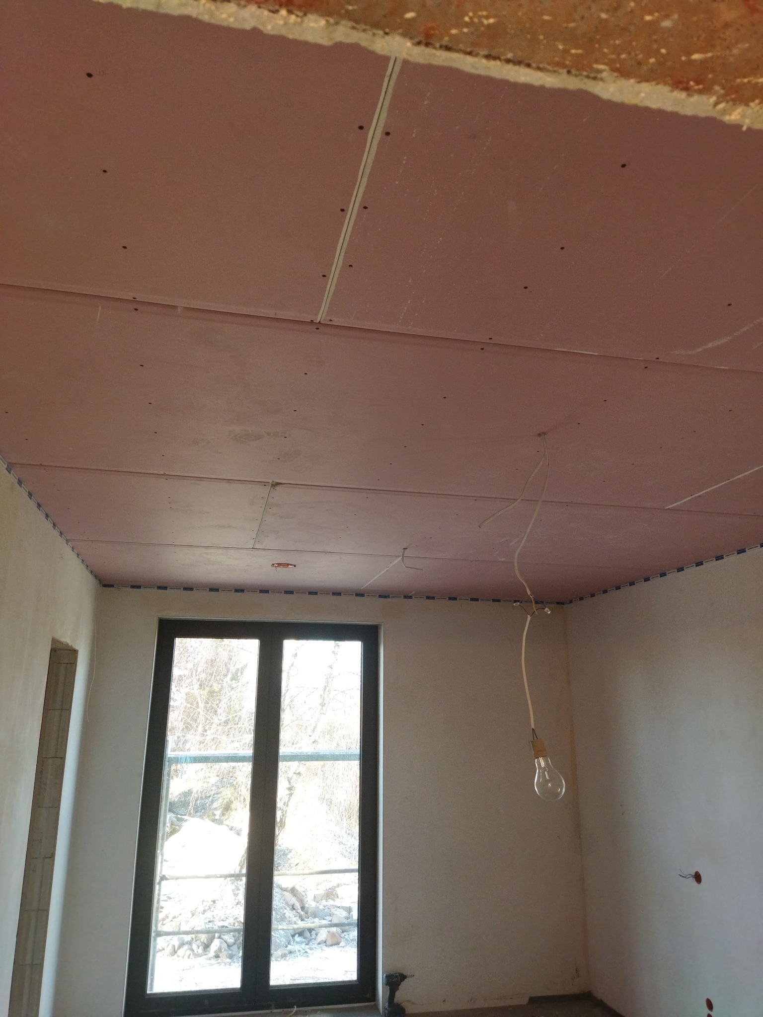 Montaż sufitu podwieszanego z płyt gipsowo-kartonowych, widoczne kable wystające z otworu, okno z widokiem na zewnątrz.