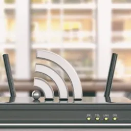 Czarny router z antenami i srebrnym symbolem Wi-Fi na tle biura z dużymi oknami, obok kubek z kolorowymi kredkami i biały głośnik.