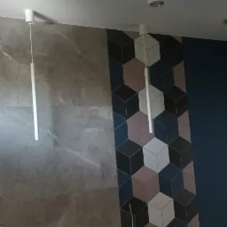 Dwie cylindryczne lampy wiszące z białymi kloszami zamontowane w łazience z szarą ścianą imitującą marmur i dekoracyjną ścianą z geometrycznymi płytkami 3D