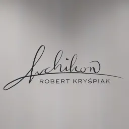 Czarny, ręcznie malowany napis 'Archihon ROBERT KRYŚPIAK' na jasnoszarej ścianie.