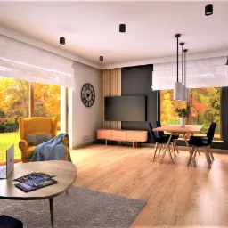 Wnętrze salonu z jadalnią w stylu nowoczesnym, z dużymi oknami z widokiem na jesienny ogród, żółtym fotelem, drewnianym stołem jadalnym i telewizorem na ścianie.