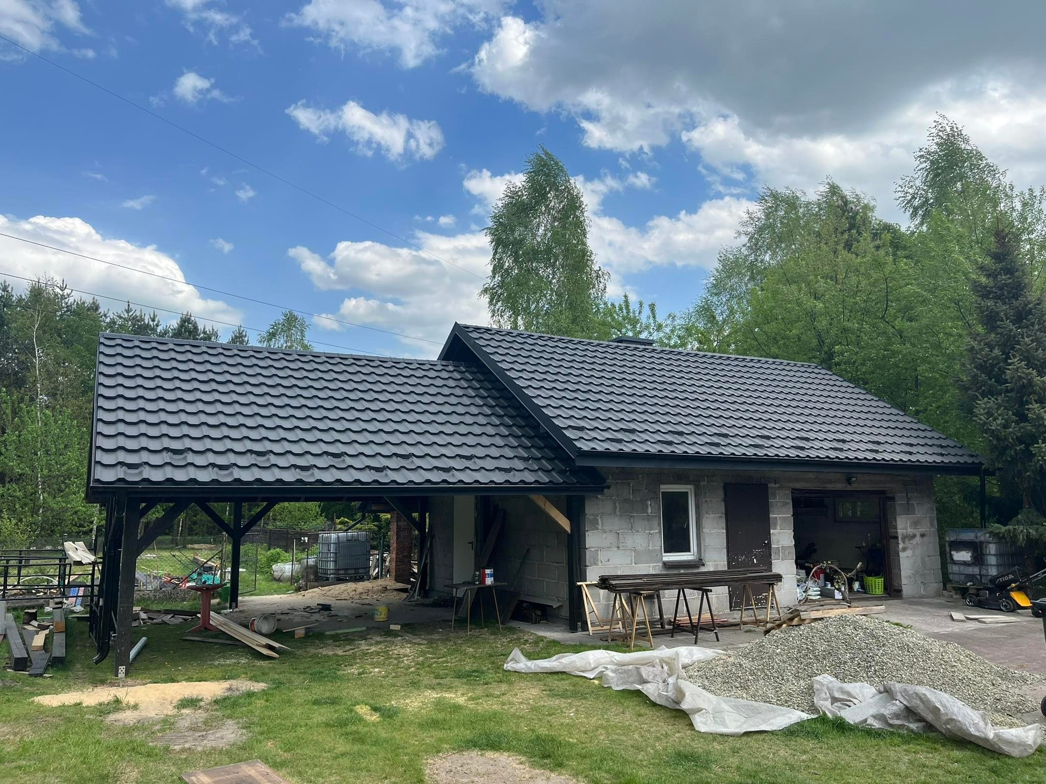 Nowy, czarny dach z dachówki modułowej na budynku gospodarczym w Chrzanowie, z widocznym przygotowaniem do dalszych prac budowlanych i stertą żwiru na trawniku.