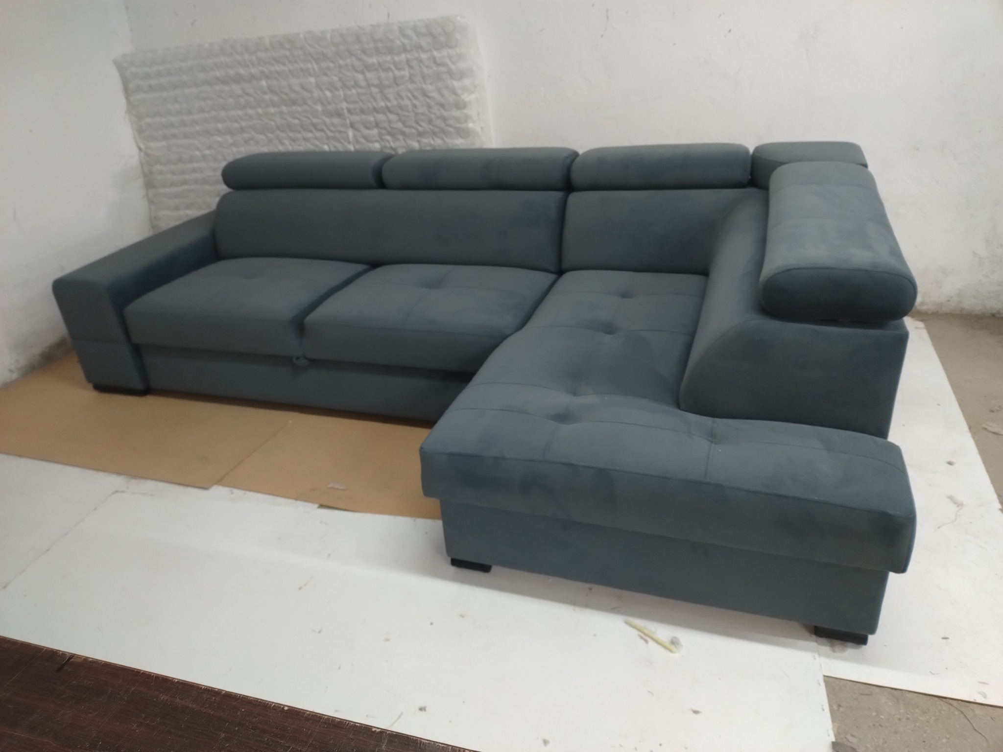 Szary narożnik z regulowanymi zagłówkami, widoczny na kartonowym podłożu w jasnym pomieszczeniu.