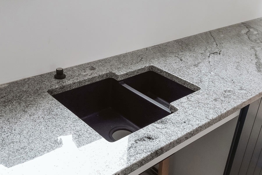 Granitowy blat z czarnym, dwukomorowym zlewem w kształcie litery L, widoczny czarny korek automatyczny