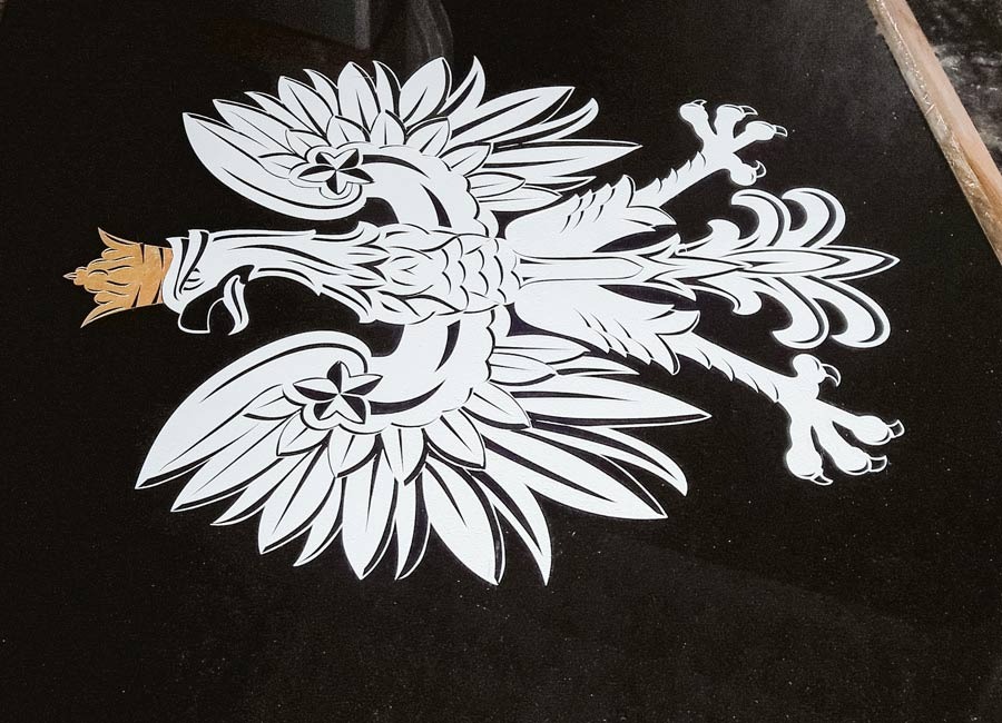 Biały orzeł w koronie z elementami złota na czarnym, błyszczącym tle.