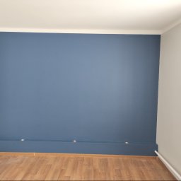 Remwik - Świeżo pomalowana na niebiesko ściana z listwą przypodłogową z wbudowanymi punktowymi lampkami, widoczny fragment parkietu i pomalowana na szaro sąsiednia ściana.