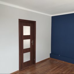 Remwik - Wnętrze po remoncie: ściany pomalowane na szaro i granatowo, brązowe drzwi z trzema szybami, drewniana podłoga.