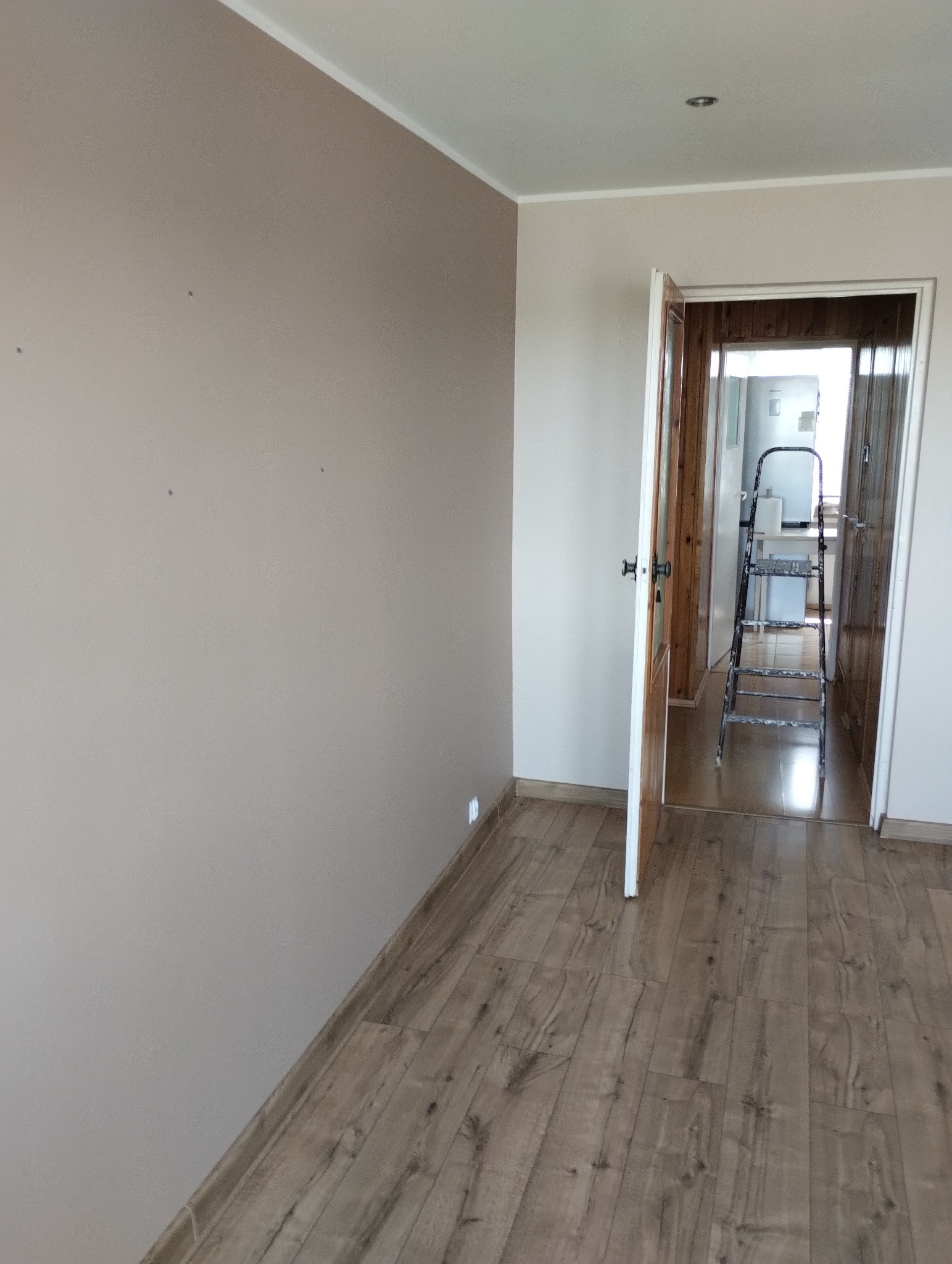 Świeżo pomalowany pokój z beżowymi ścianami i drewnianą podłogą, widoczne ślady po szpachlowaniu, drabina w przejściu do kuchni.