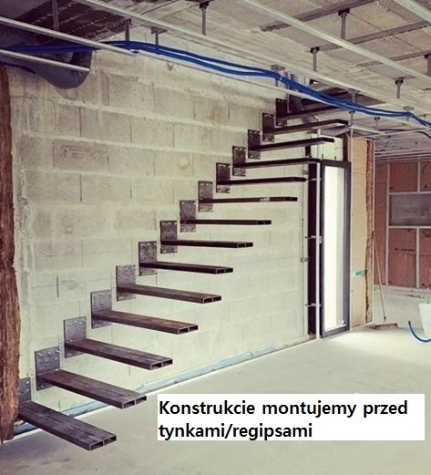 Montaż metalowych stopni schodów wspornikowych na surowej ścianie z pustaków, widoczne mocowania przed tynkowaniem.