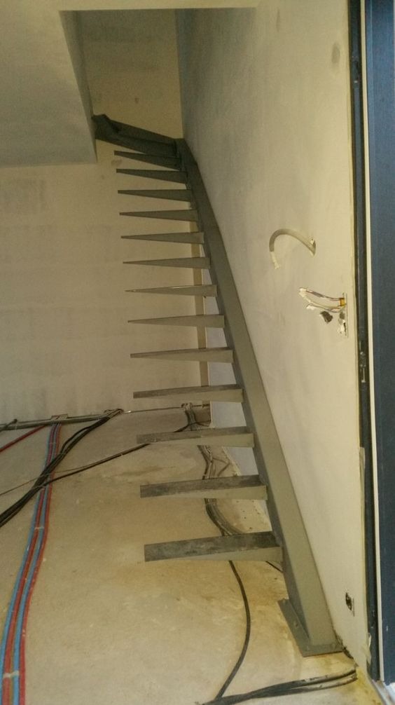 Montaż minimalistycznych, metalowych schodów w surowym stanie w budynku we Wrocławiu, widoczne kable i instalacje w trakcie prac wykończeniowych.