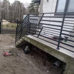 KM Patryk Szymański - Nowoczesna, grafitowa balustrada schodowa z geometrycznym wzorem, zamontowana przy wejściu do domu. Widoczne narzędzia sugerują trwający montaż.