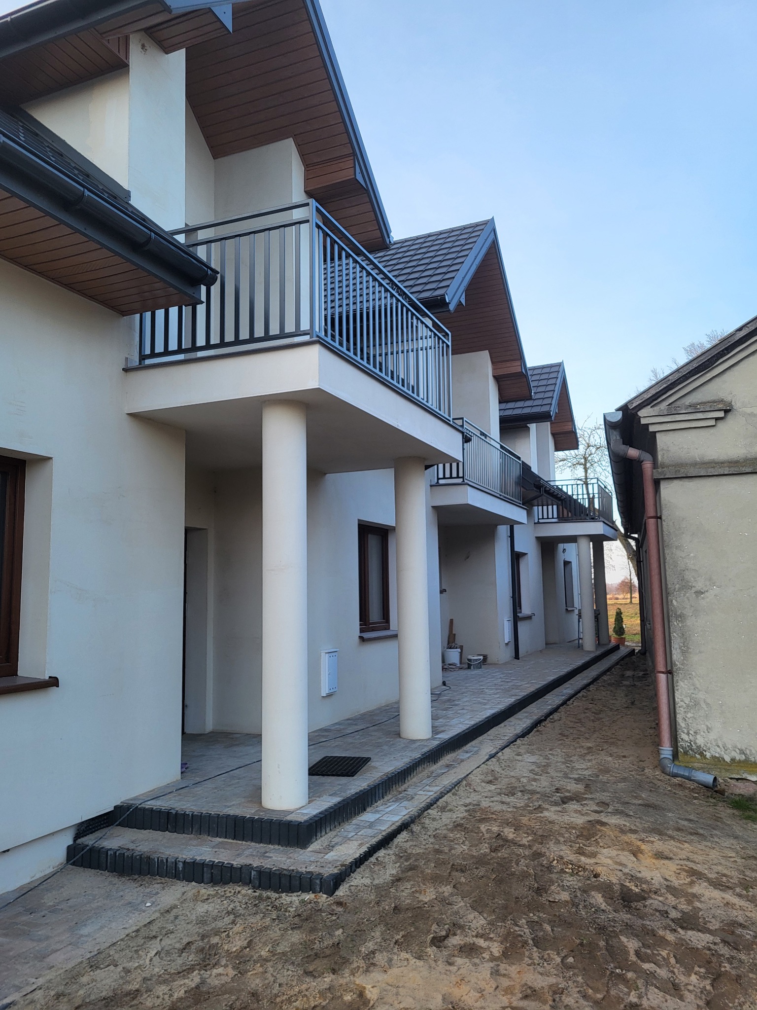 Szeregówka z balkonami i czarnymi balustradami. Kolumny podtrzymujące balkony. Widok z dołu na nowo wybudowane domy.