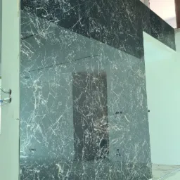 Ściana wyłożona dużymi, czarnymi płytami z białym marmurkowym wzorem, widoczne gniazdka elektryczne i niedokończone wykończenie sufitu.