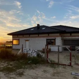 Dom jednorodzinny w trakcie budowy w Bydgoszczy, widok z zewnątrz o zachodzie słońca, z widocznymi bloczkami i niedokończonymi oknami.