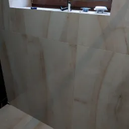 Wykończona ściana i podłoga w łazience z beżowych płytek imitujących marmur, widoczne akcesoria montażowe oświetlenia na parapecie okna.