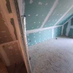T.X.Servise - Poddasze w trakcie remontu: ściany i sufit pokryte płytami gipsowo-kartonowymi, widoczne łączenia płyt przygotowane do szpachlowania, fragment schodów i instalacji wentylacyjnej.