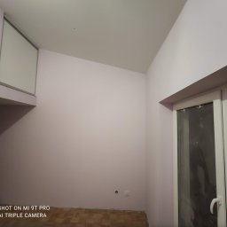 T.X.Servise - Pomalowane na jasny róż ściany w pokoju z drewnianą podłogą, widoczne okno z białymi ramami i nisko umieszczone gniazdko elektryczne.