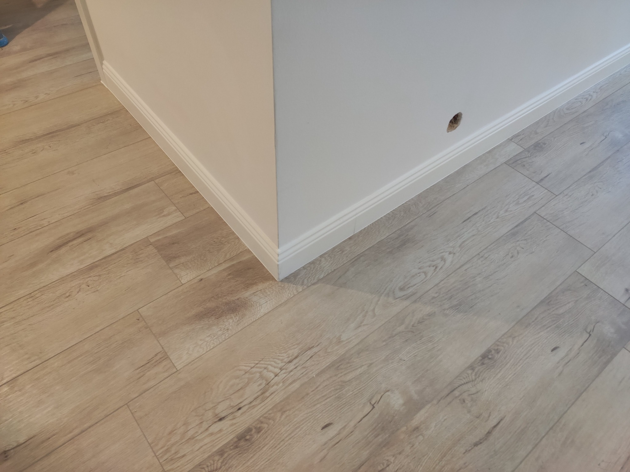 Fragment pokoju po remoncie: jasne panele podłogowe imitujące drewno, biała ściana z listwą przypodłogową i otworem po gniazdku.