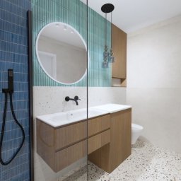 SofiJA Zofia Stanek - Nowoczesna łazienka z niebieskimi i zielonymi płytkami, okrągłym lustrem i drewnianą szafką pod umywalką. Uwagę przykuwają wiszące lampy i podłoga w stylu lastryko.