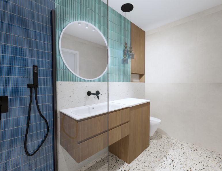 Nowoczesna łazienka z niebieskimi i zielonymi płytkami, okrągłym lustrem i drewnianą szafką pod umywalką. Uwagę przykuwają wiszące lampy i podłoga w stylu lastryko.