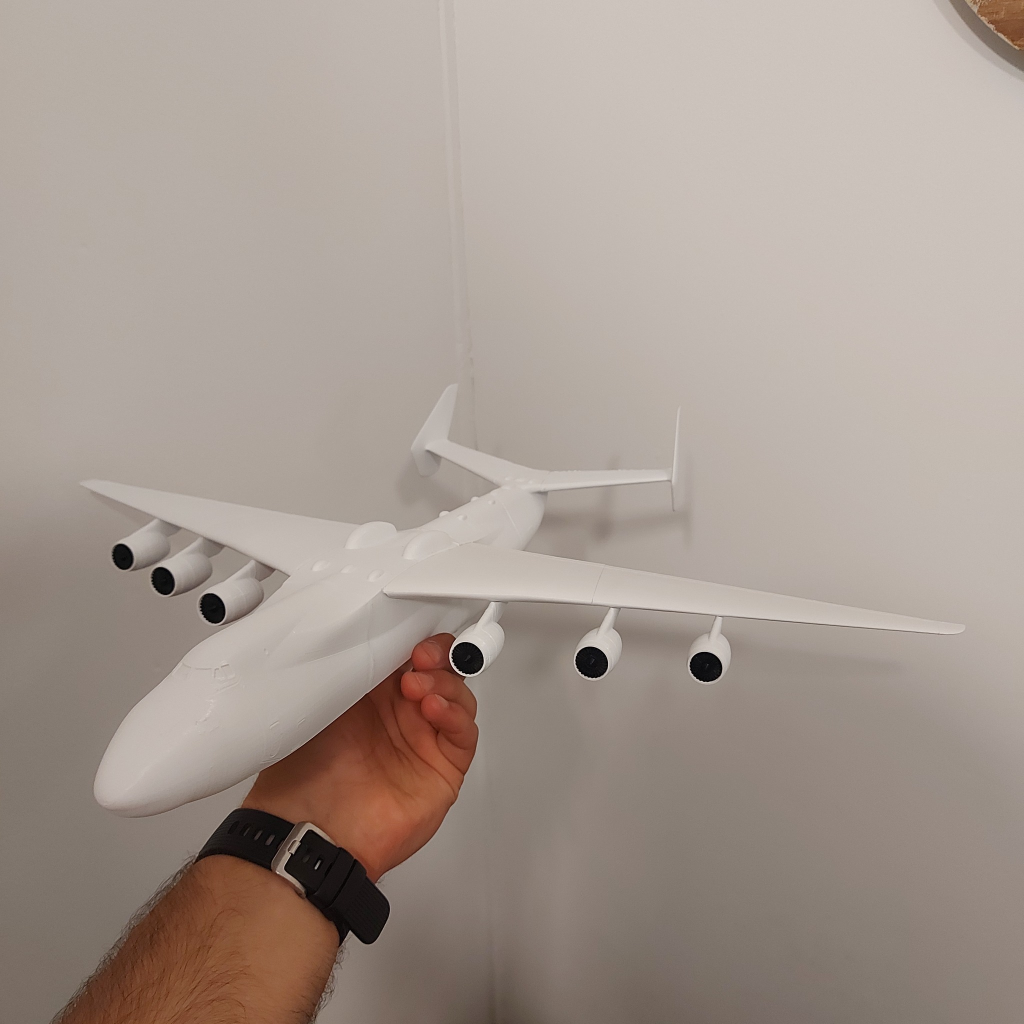Biały model samolotu An-225 Mrija trzymany w dłoni, widoczne sześć silników pod skrzydłami i czarny zegarek na nadgarstku.