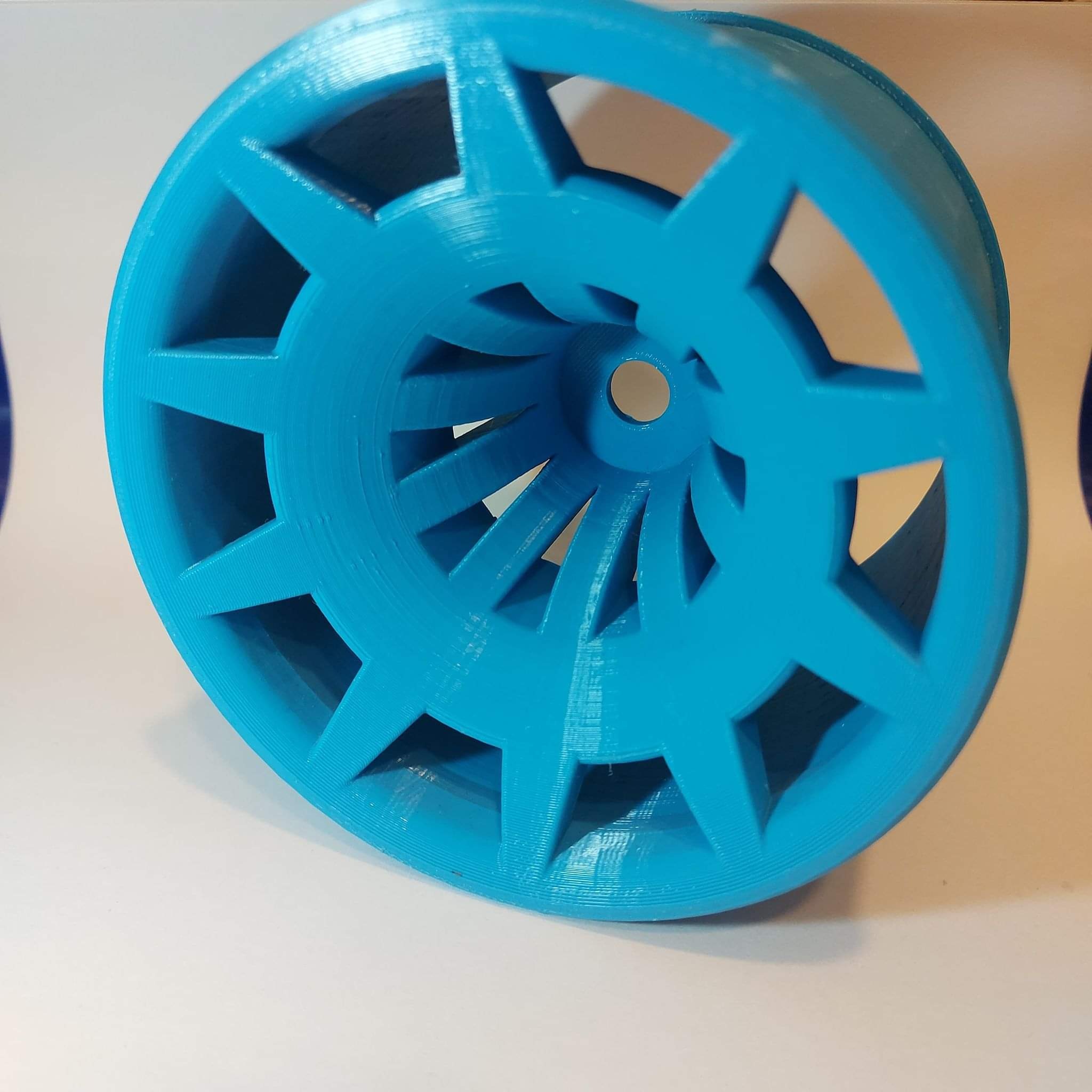 Turkusowy element 3D drukowany z otworami w kształcie gwiazd, widoczne warstwy druku, centralny otwór, na białym tle.