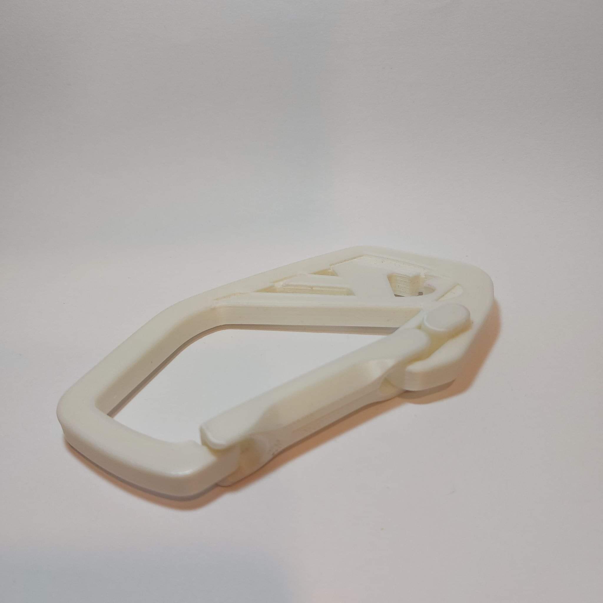 Biały plastikowy karabińczyk z widocznymi warstwami druku 3D, leżący na białym tle.