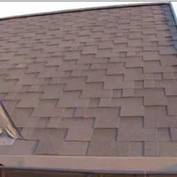 Fragment brązowego dachu pokrytego gontem bitumicznym, widoczny z boku, z rynną i obróbką blacharską w kolorze szarym.